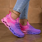 Woman adjusting the heel of a pink and purple knit trainer while seated outdoors on stone paving