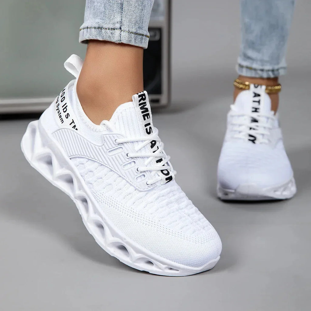 Side view of a white knit trainer with black lace-up panel and woven mesh upper, worn on foot