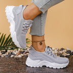 Side view of grey knit trainers with white sole worn on foot, shown with a height marker of the sole