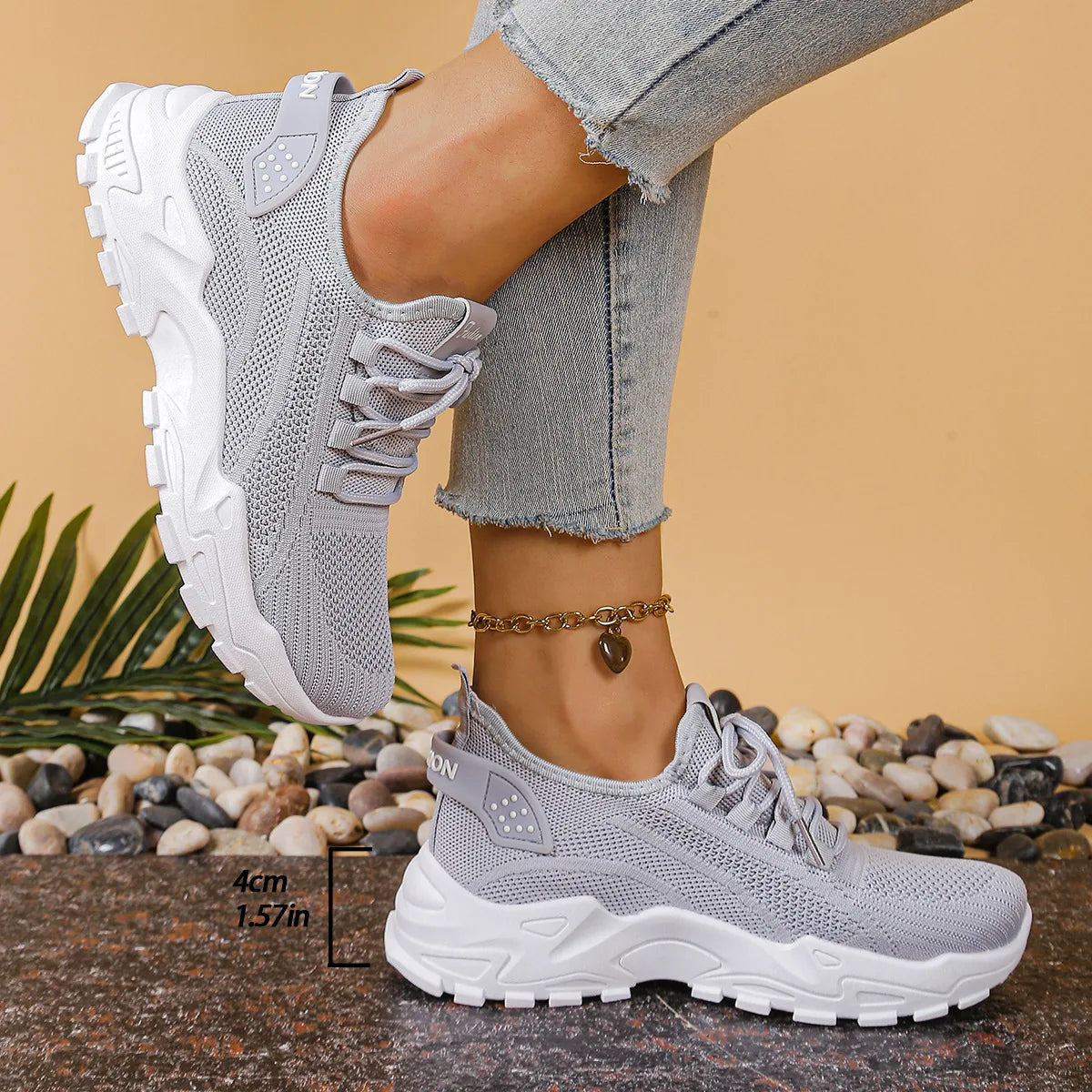 Side view of grey knit trainers with white sole worn on foot, shown with a height marker of the sole