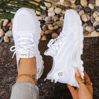 Overhead view of white knit trainers with white sole and fabric loop tab, one shoe held by hand
