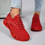 Angled side view of a red knit trainer with contrast black laces and wavy blade outsole, worn outdoors