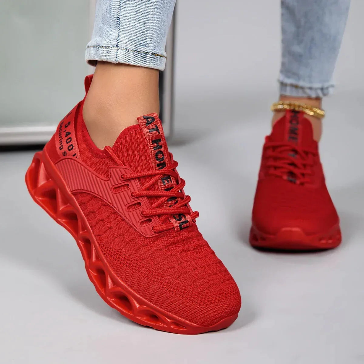 Angled side view of a red knit trainer with contrast black laces and wavy blade outsole, worn outdoors