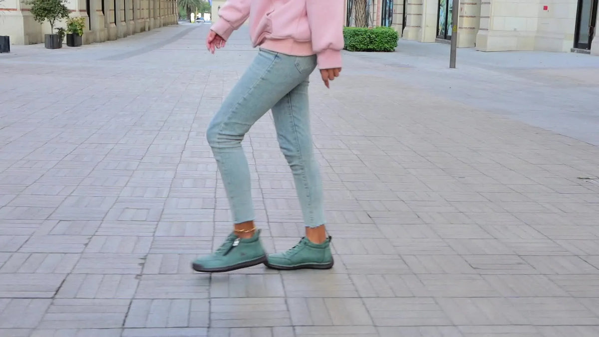 Grey suede ankle trainer lifted mid-stride, showing the ribbed sole and heel pull loop