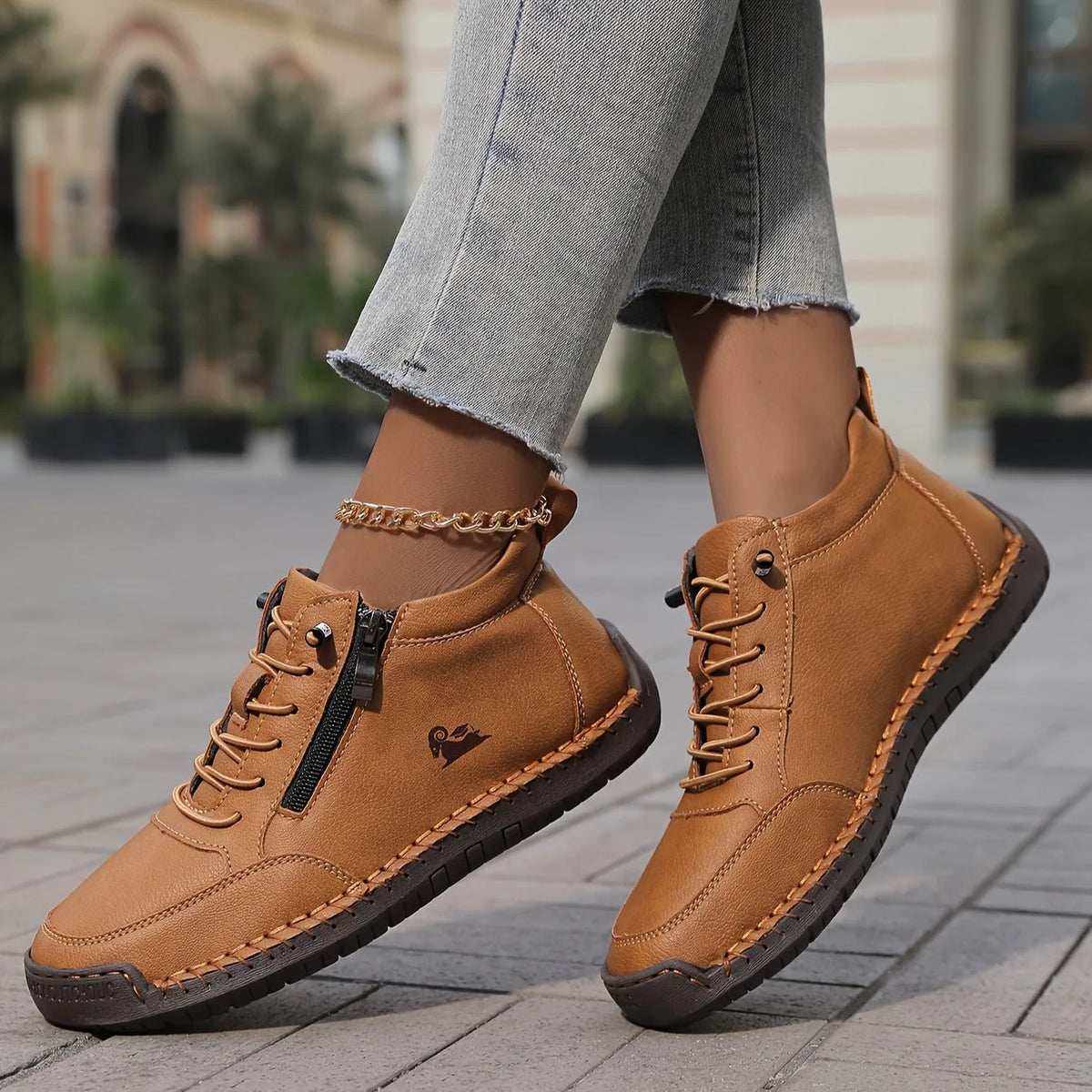 Tan brown leather high-top trainer with zip pull, lace-up front and contrast topstitching worn on cobbled street