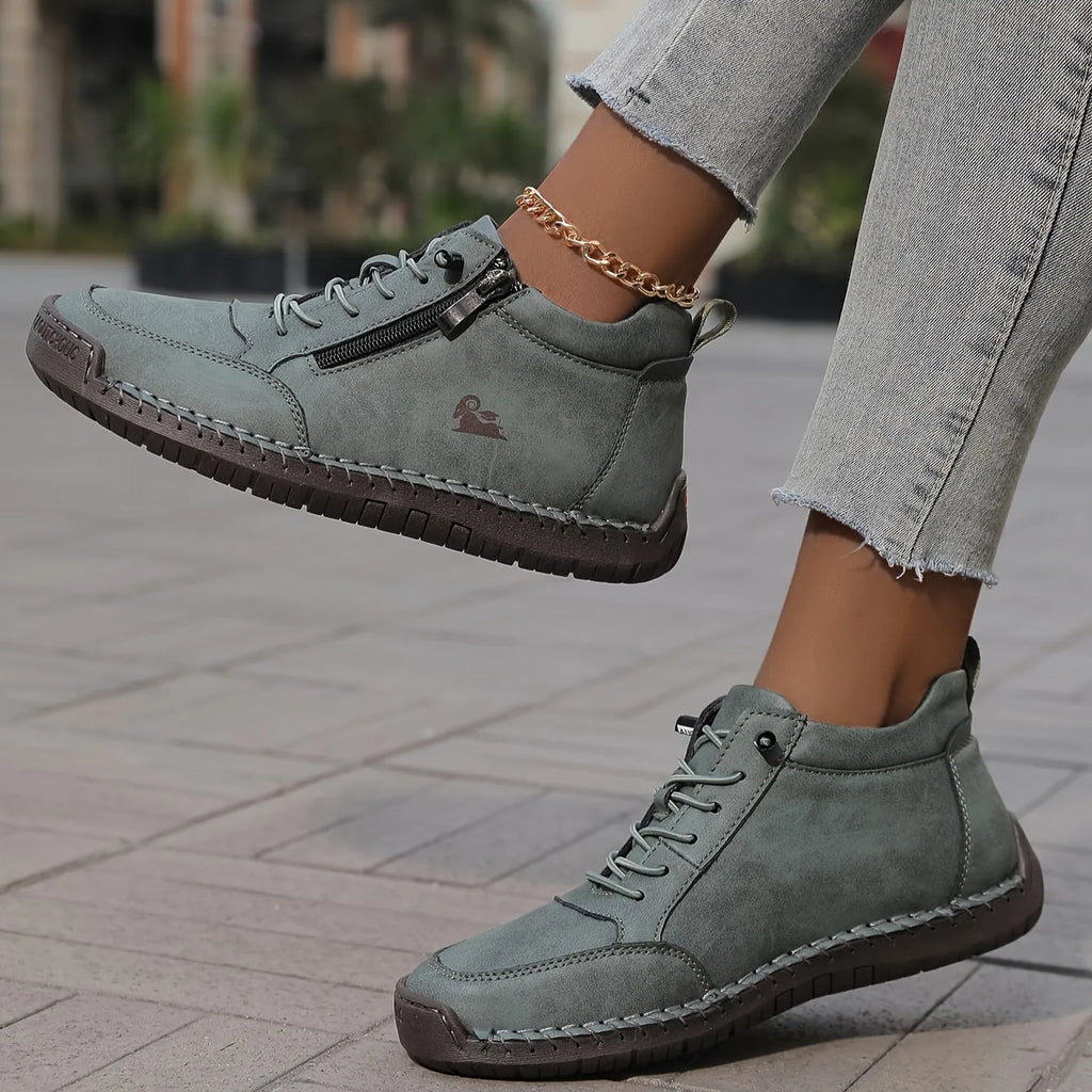 Close-up side profile of sage grey-green leather ankle sneaker lifted mid-step, showing ribbed rubber sole