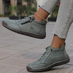 Close-up side profile of sage grey-green leather ankle sneaker lifted mid-step, showing ribbed rubber sole