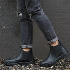 Person wearing black Chelsea boots with cuffed jeans, standing on scrap metal to show outdoor durability