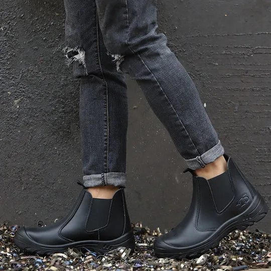 Person wearing black Chelsea boots with cuffed jeans, standing on scrap metal to show outdoor durability