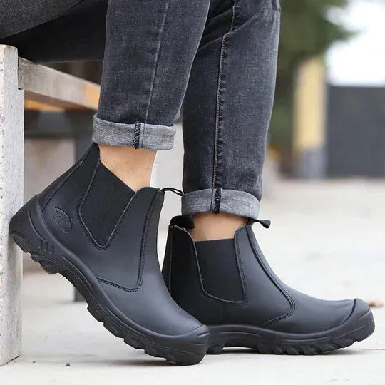 Close-up of black Chelsea boots worn with rolled jeans while seated, highlighting the ankle fit and pull tabs