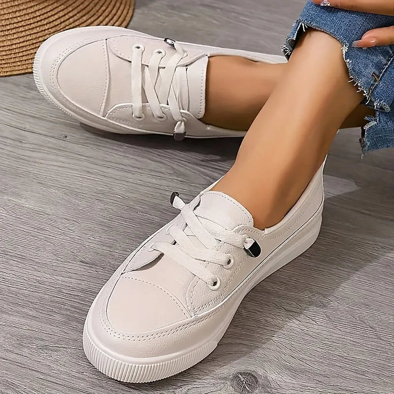 Close-up side view of white leather lace-up trainers worn with cropped denim jeans, showing the cushioned platform sole