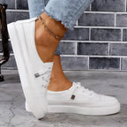 Side profile of a white leather trainer with stacked platform sole and metal lace-tag detail, worn with ripped jeans and an anklet
