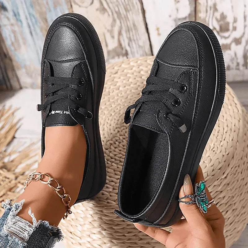 Pair of black leather lace-up trainers with ribbed platform soles, one shoe held in hand to show the stitched toe cap