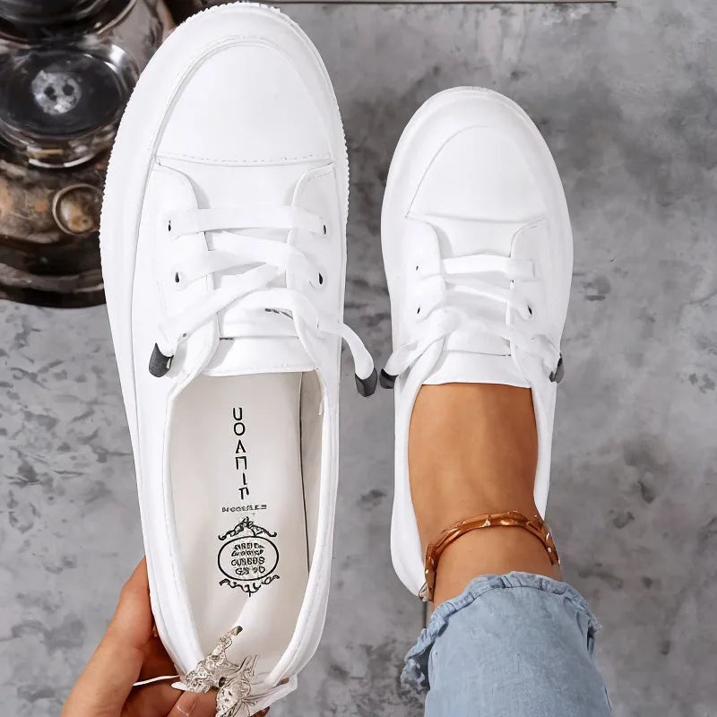Top-down view of a pair of white leather trainers with laces undone, showing the round toe and branded insole