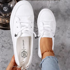 Top-down view of a pair of white leather trainers with laces undone, showing the round toe and branded insole