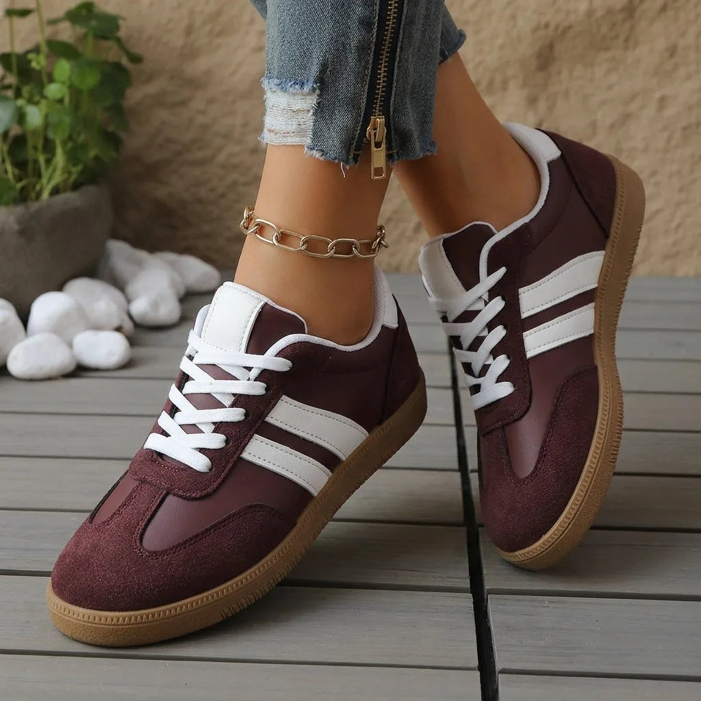 Close-up of maroon trainers crossing at the ankle, showing white stripe panel and ribbed heel trim