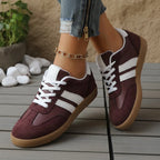 Close-up of maroon trainers crossing at the ankle, showing white stripe panel and ribbed heel trim
