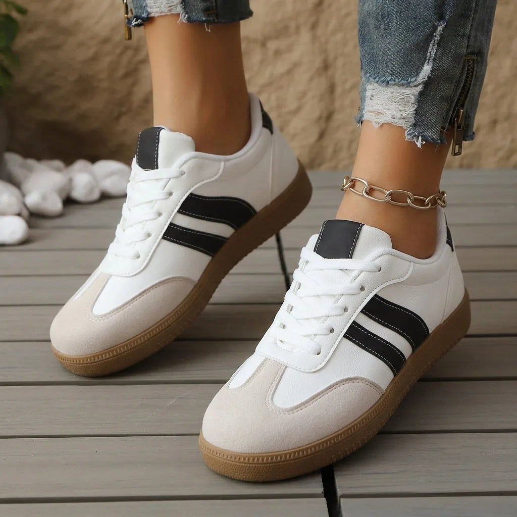 Front angled view of maroon and cream striped trainers with white laces on a wooden deck