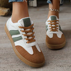 Green and white trainers with tan suede toe caps and contrasting laces, worn outdoors on a wooden deck