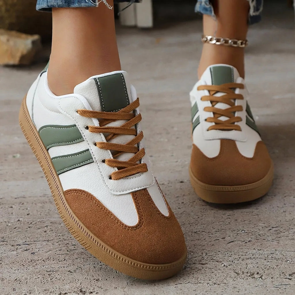 Green and white trainers with tan suede toe caps and contrasting laces, worn outdoors on a wooden deck