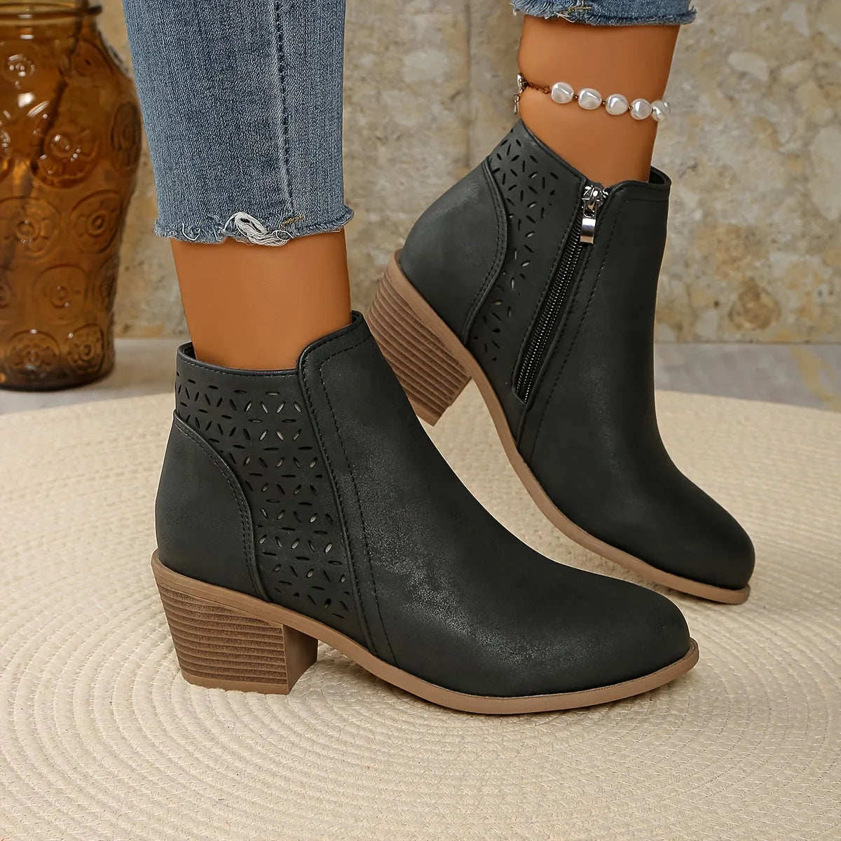 Side view of black perforated ankle boots with stacked block heel worn with cropped jeans and pearl anklet