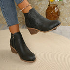 Black ankle boots with perforated pattern shown mid-step, highlighting stacked wooden-effect heel