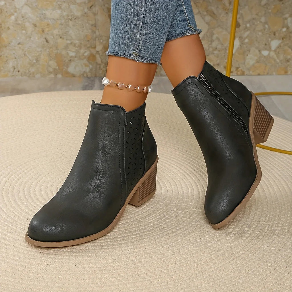 Overhead flat lay of navy blue perforated ankle boots with tan stacked heel held in hand