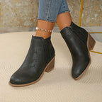 Overhead flat lay of navy blue perforated ankle boots with tan stacked heel held in hand