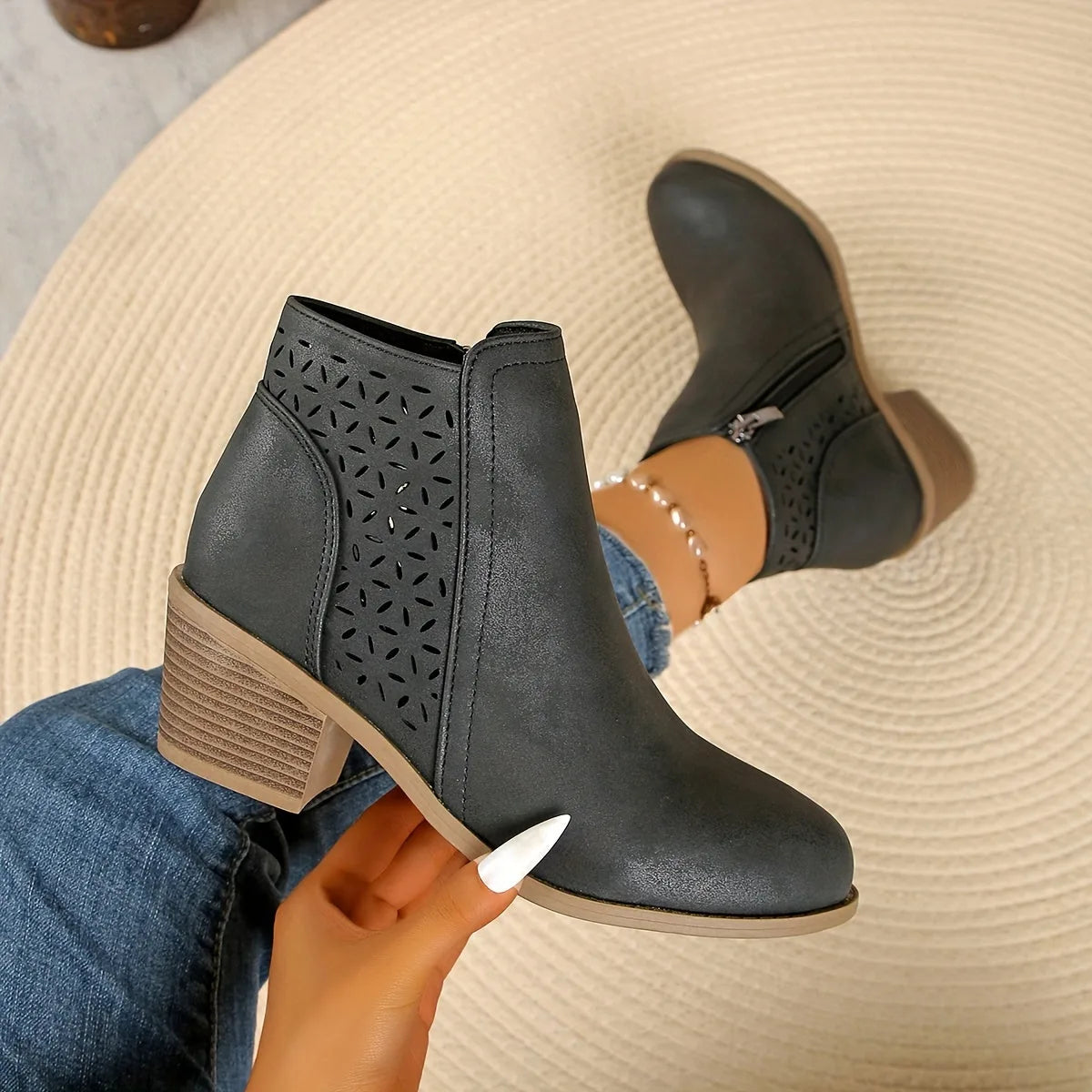 Front-on view of black cut-out ankle boots on model standing on round woven rug