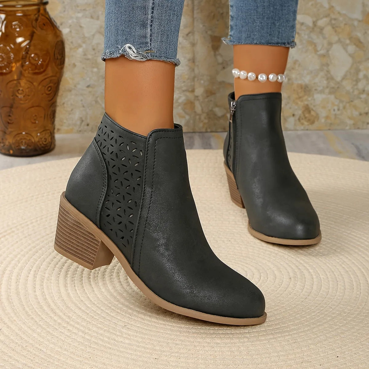 Overhead view of black ankle boots with laser-cut panel and side zip, one boot raised mid-air