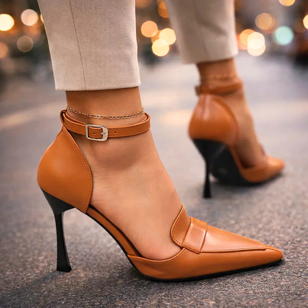 Close-up side view of tan pointed-toe heels with buckled ankle strap, worn with cream tailored trousers