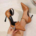 Overhead shot of tan pointed-toe heels with ankle strap held in hand, showing sole and insole detail