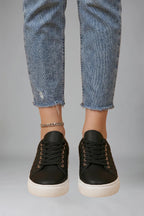 Close-up front view of black quilted trainers worn with cropped jeans and a silver anklet
