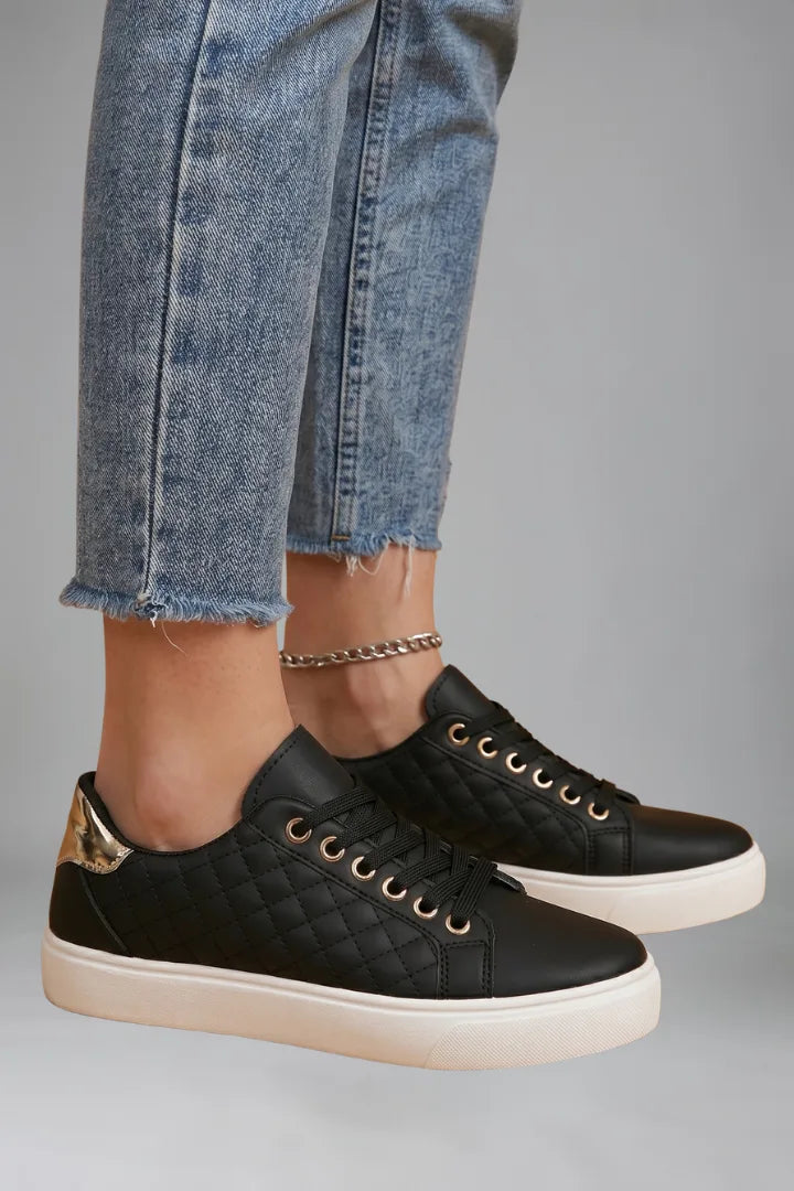 Angled side view of black quilted trainers worn with cropped jeans, showing white sole detail
