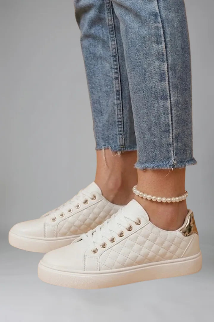 Side view of white quilted trainers with gold eyelets and metallic gold heel accent
