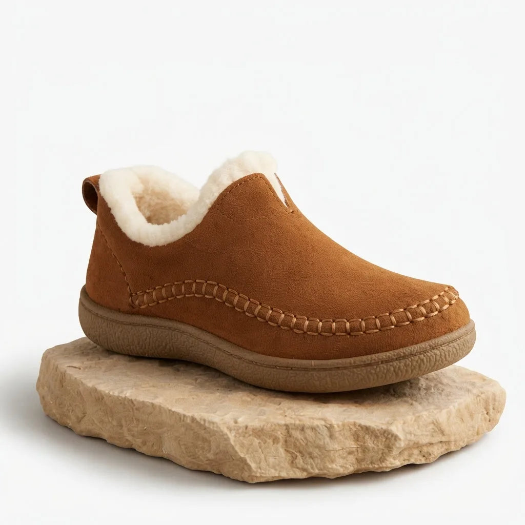 Three-quarter view of the tan suede slip-on boot resting on a stone slab, showing the gum-coloured rubber sole