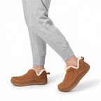 Close-up of a model wearing the tan shearling-lined slip-on boots with grey joggers, walking indoors