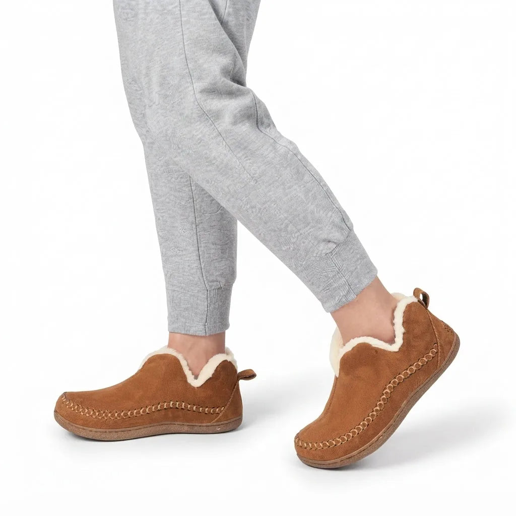Close-up of a model wearing the tan shearling-lined slip-on boots with grey joggers, walking indoors