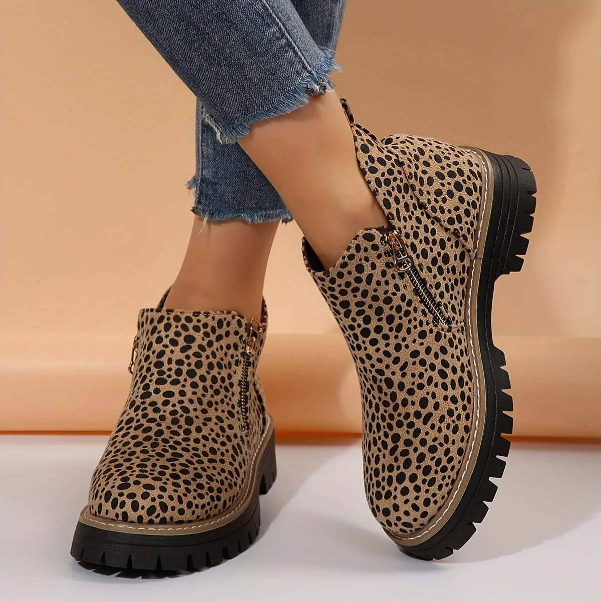 Side profile of leopard print ankle boot with gold side zip and chunky lugged black platform sole, worn crossed at the ankle
