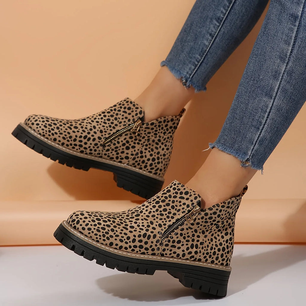 Close-up side view of leopard print ankle boots showing the gold zip pull and ribbed sole detail on model's feet