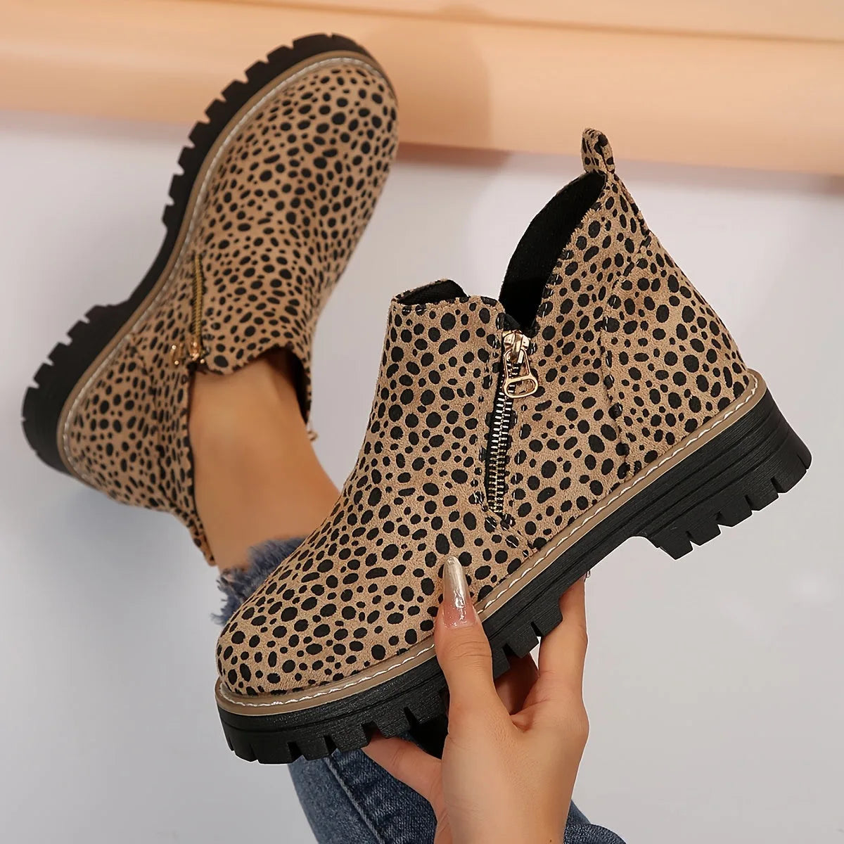 Pair of leopard print ankle boots held in hand, showing the textured lugged outsole and soft suede-look upper