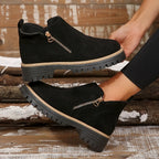 Side view of black ankle boots held by hand, highlighting the gold zip, tan trim and thick grooved platform sole