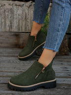 Dark olive green ankle boots with gold side zip worn on feet, shown from the side against a weathered backdrop
