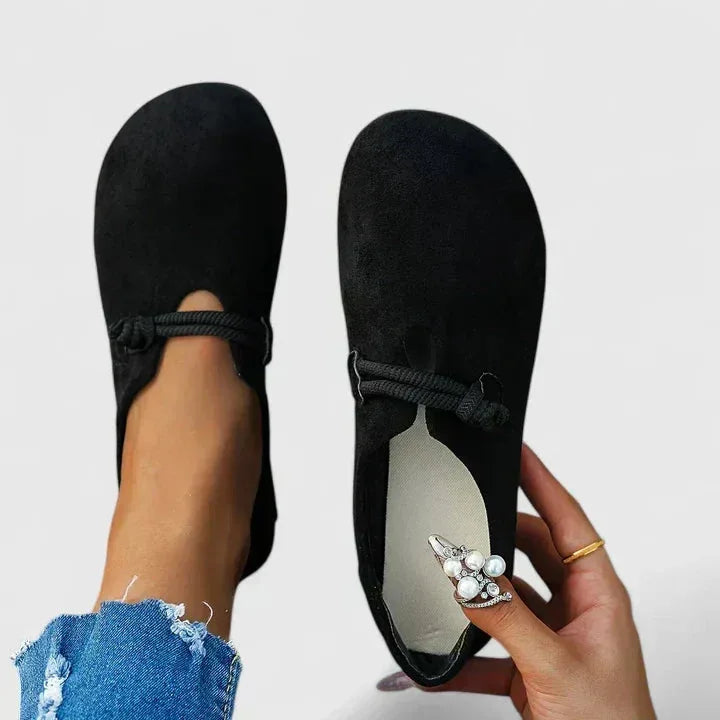 Top-down view of black suede slip-on flats with corded rope trim held in hand to show the cushioned footbed