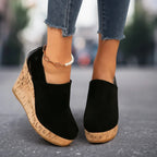 Close-up rear detail of black suede wedge bootie with glossy patent heel counter and textured cork wedge sole
