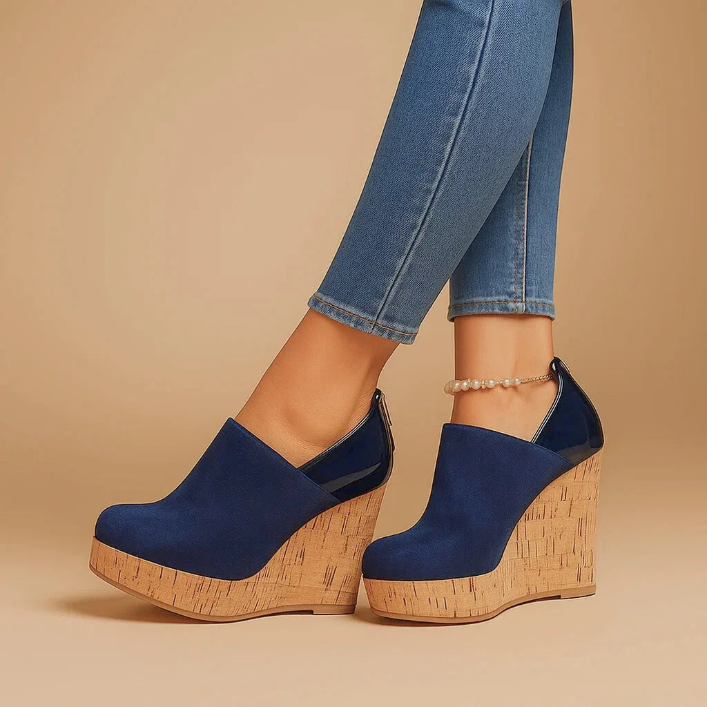 Studio side profile of navy suede wedge ankle boots on a beige background, showing the rounded toe and cork platform heel