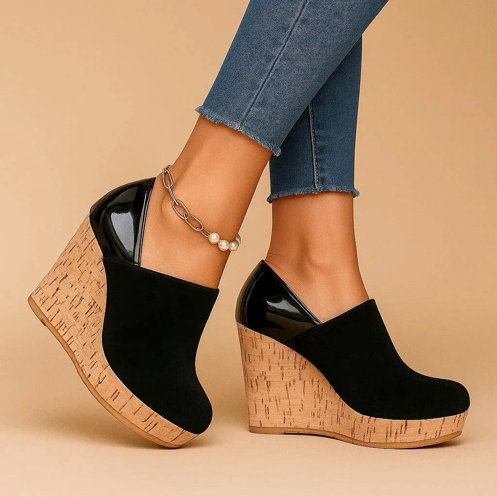 Studio side profile of black suede wedge ankle boots on a beige background, showing the patent trim and layered cork wedge