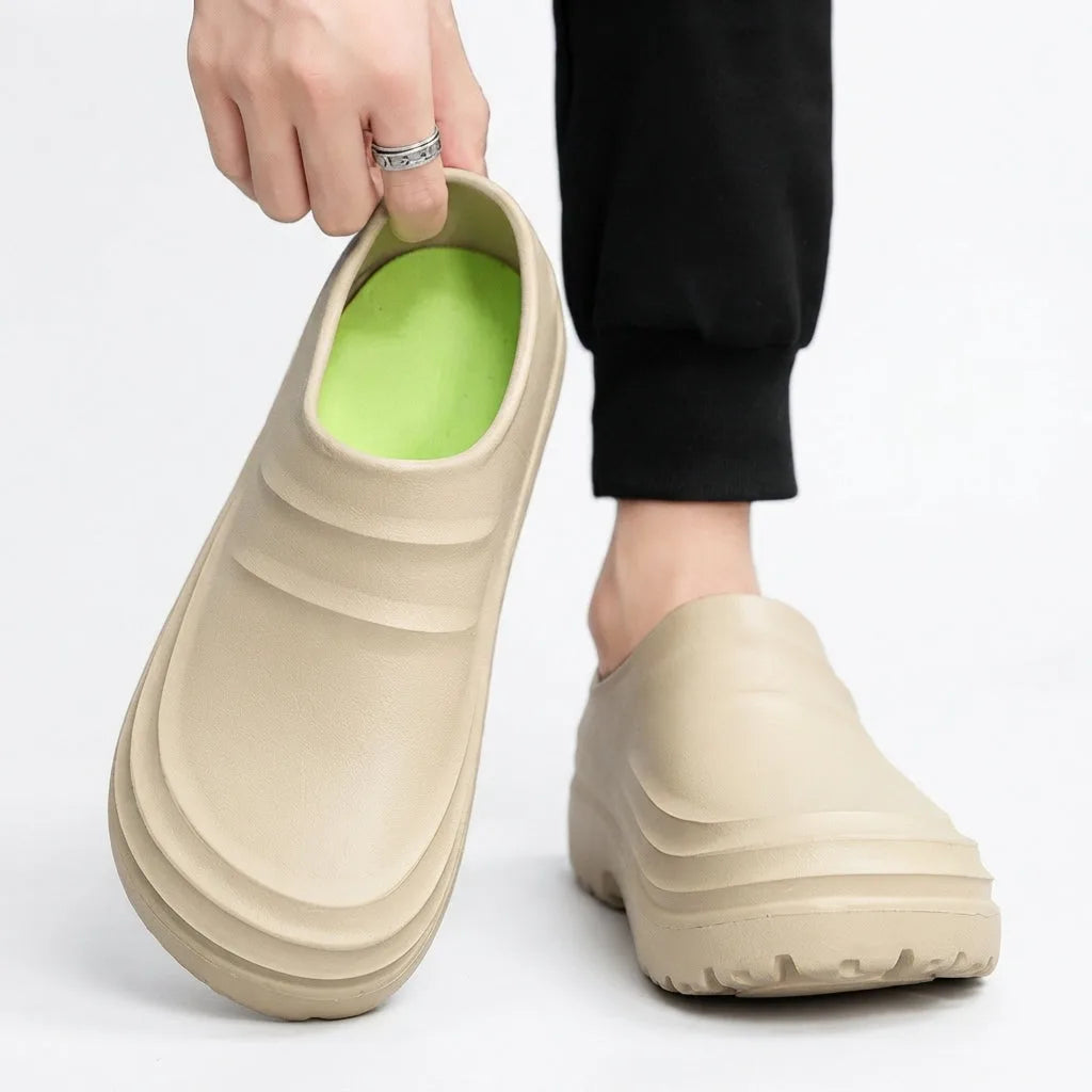 Close-up of hand lifting a beige clog to reveal its soft green inner footbed while worn on the other foot