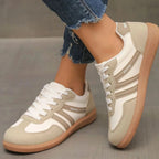 Beige and taupe lace-up trainers worn on foot, side view showing striped panel detail and gum sole