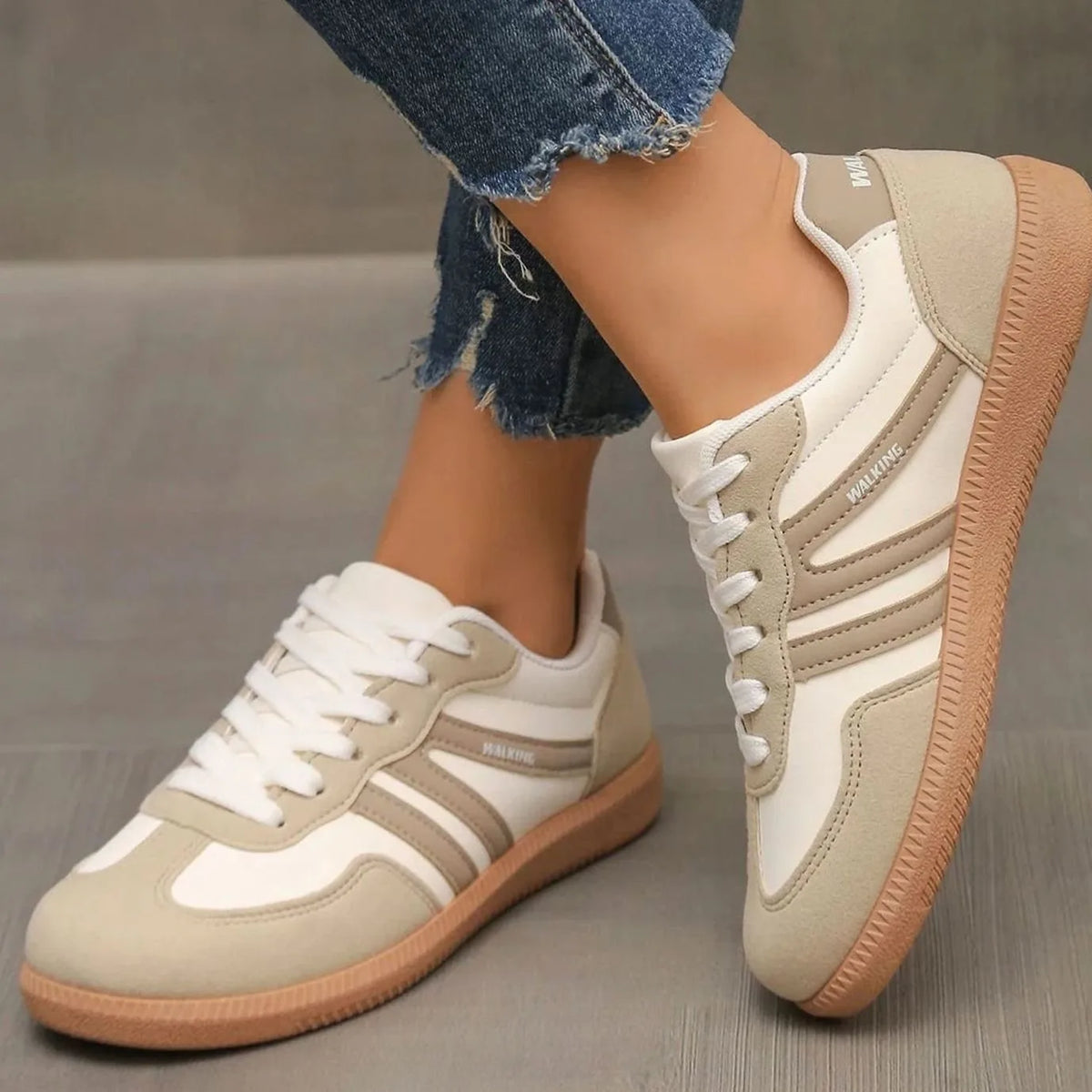 Beige and taupe lace-up trainers worn on foot, side view showing striped panel detail and gum sole